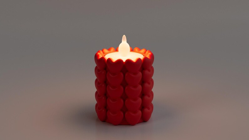 May include: A red candle with a heart-shaped design. The candle has a white, flickering LED light. The candle is cylindrical and sits on a gray surface. The candle is a decorative item.