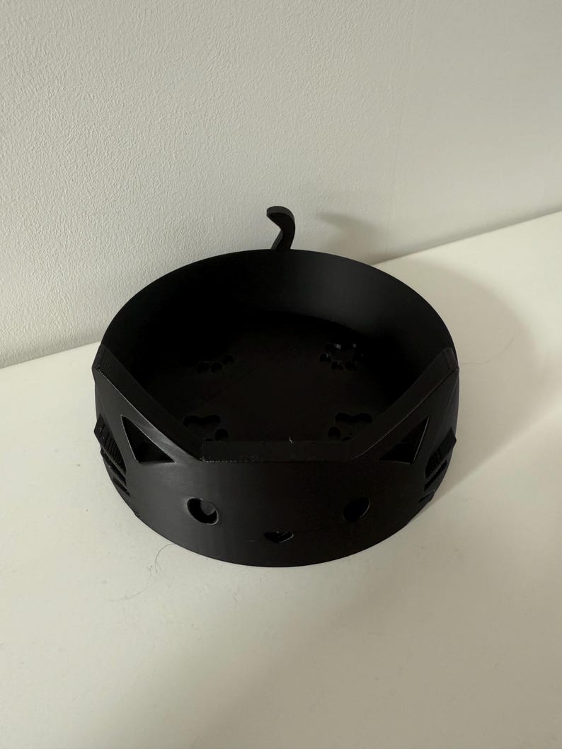 Puede incluir: Un cuenco negro de metal con forma de gato. El cuenco tiene cortes para los ojos y la nariz, con una peque&ntilde;a cola que se extiende desde la parte superior. El cuenco es redondo con una base plana y est&aacute; dise&ntilde;ado para guardar objetos peque&ntilde;os.