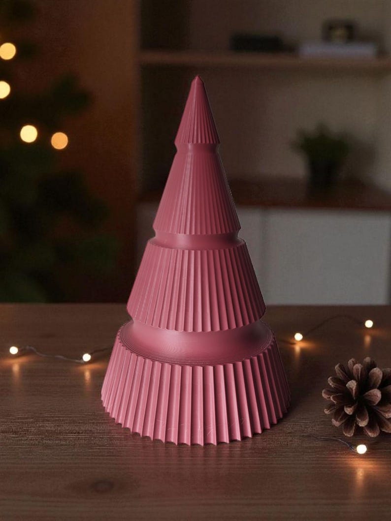 May include: A pink, stylized Christmas tree decoration with a ribbed design. The tree is on a wooden surface, with a pine cone and string lights nearby. The tree has a conical shape with layered sections.