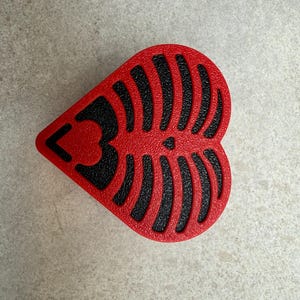 May include: A heart-shaped, red object with a black, textured design resembling a rib cage. The number "3" is visible on the left side of the heart. The object is likely a decorative item or a component of a larger design.