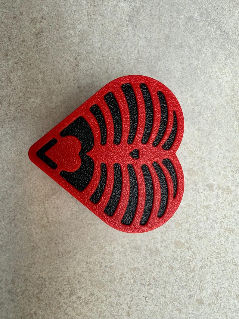 May include: A heart-shaped, red object with a black, textured design resembling a rib cage. The number "3" is visible on the left side of the heart. The object is likely a decorative item or a component of a larger design.