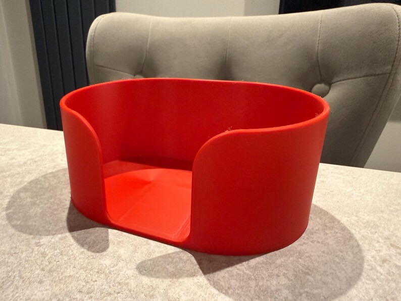May include: A bright red, rectangular container with rounded corners. The container has a low profile and is open at the top, with a curved cutout on each side. The container is sitting on a light gray surface.
