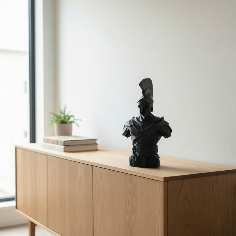 May include: A black sculpture of a Spartan warrior, featuring a helmet and armour. The bust is placed on a light wood cabinet. A small plant and books are visible in the background. A decorative item.