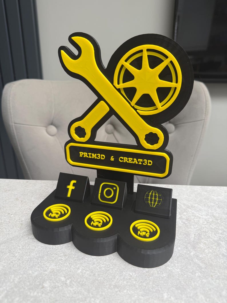 May include: A black and yellow 3D-printed display stand featuring a wrench, a wheel, and social media icons. The stand includes the text "PRIM3D & CREAT3D" and NFC symbols.
