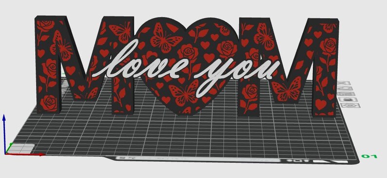 May include: A 3D-printed decorative piece spelling "MOM" with a heart-shaped "O". The letters and heart are black with red butterfly, rose, and heart patterns. The words "love you" are in cursive.