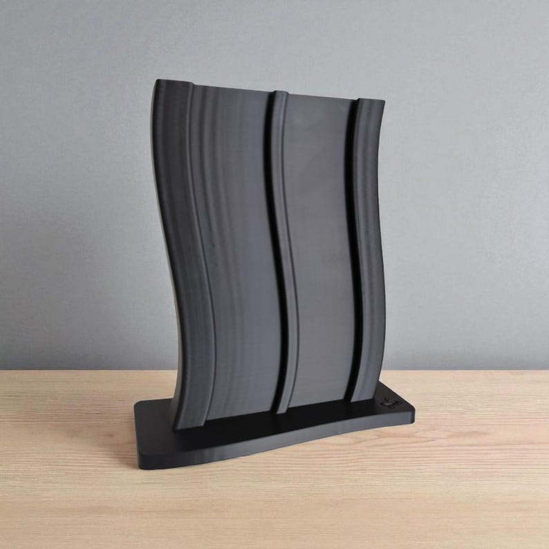 May include: A black, curved decorative item featuring three vertical grooves. The object is made of a solid material and rests on a rectangular base. The design has a modern, minimalist aesthetic, and is displayed on a wooden surface.