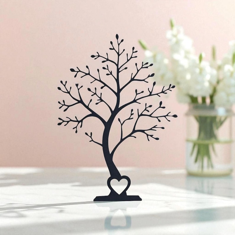 May include: A black metal tree-shaped jewelry holder with a heart-shaped base. The tree has many branches and small leaves. The background is a soft pink, with a vase of white flowers to the right.