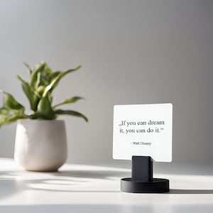 May include: A white card with the quote "If you can dream it, you can do it." by Walt Disney, held in a black stand. A small potted plant is in the background.