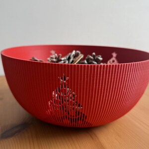 Puede incluir: Un cuenco decorativo rojo con una textura acanalada y un dise&ntilde;o recortado de &aacute;rbol de Navidad. El cuenco contiene varios conos de pino. Este cuenco festivo es adecuado para la decoraci&oacute;n de temporada.