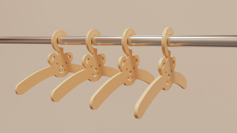 Pu&ograve; includere: Quattro grucce di legno per bambini con un design a forma di orsetto. Le grucce sono di colore beige chiaro e sono appese a un'asta di metallo argentato. Lo sfondo &egrave; di colore beige chiaro.