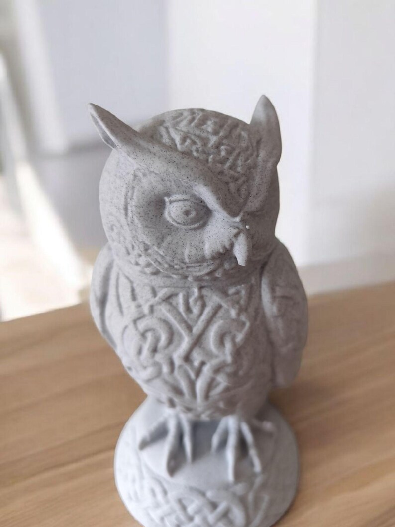 May include: A gray owl figurine with detailed feather and wing patterns. The owl has large eyes and a small beak. The figurine is made of a stone-like material and sits on a round base. The owl's chest features an intricate design.