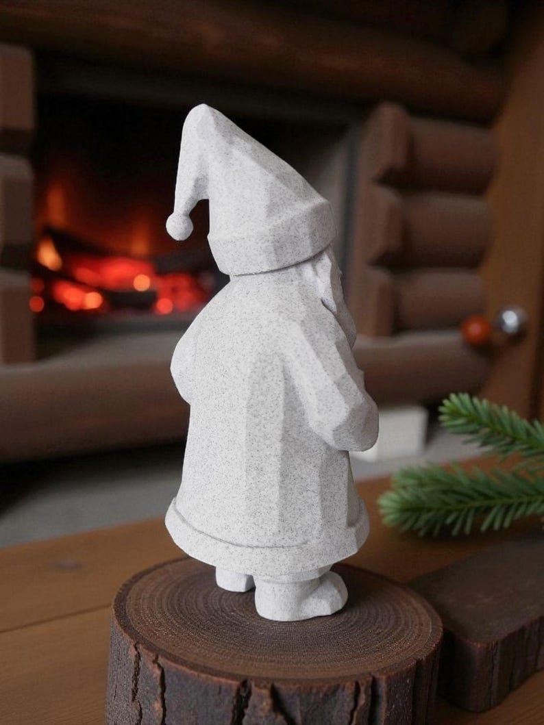 K&ouml;nnte beinhalten: Eine graue, geometrische Weihnachtsmannfigur mit spitzem Hut und Mantel, die auf einer Holzscheibe steht. Die Figur hat eine strukturierte Oberfl&auml;che und steht vor einem Kamin.