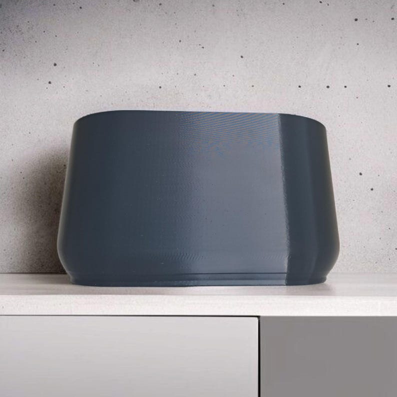 Puede incluir: Una maceta moderna de color gris oscuro con forma rectangular redondeada. La maceta tiene un acabado liso y mate y est&aacute; sobre una superficie blanca. El dise&ntilde;o es minimalista y adecuado para uso en interiores o exteriores.
