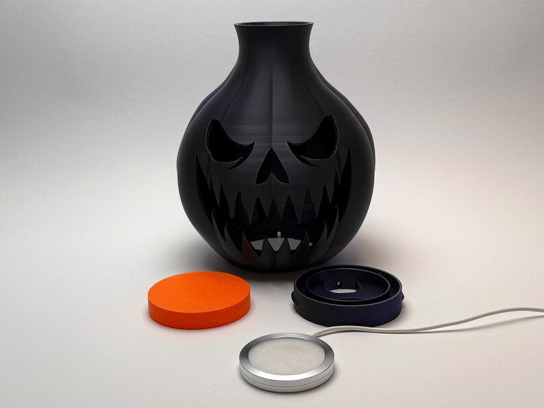 Puede incluir: Un jarr&oacute;n decorativo negro con forma de calabaza con una cara tallada, perfecto para Halloween. Incluye un disco naranja, un anillo negro y una luz plateada con un cable blanco. El jarr&oacute;n tiene una boca ancha y una superficie texturizada.