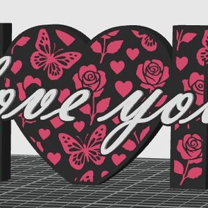 May include: A decorative sign spelling "MOM" with a heart in the center. The letters and heart are black with pink butterfly, rose, and heart patterns. The words "love you" are written in white across the heart.