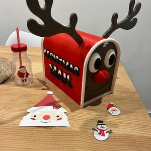 May include: A red Christmas mailbox with reindeer antlers, the words "CHRISTMAS MAIL" in black, and a reindeer face. A Santa Claus-themed drinking bottle and Christmas-themed cutouts of Santa and a snowman are also present.