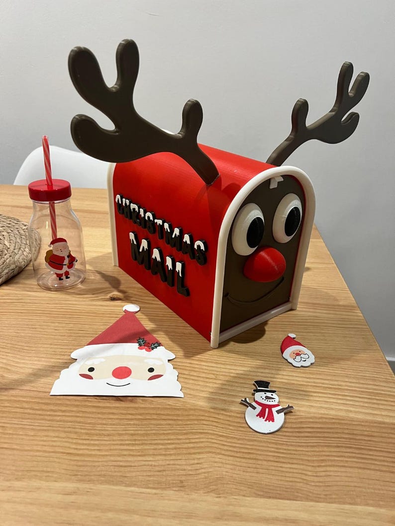 May include: A red Christmas mailbox with reindeer antlers, the words "CHRISTMAS MAIL" in black, and a reindeer face. A Santa Claus-themed drinking bottle and Christmas-themed cutouts of Santa and a snowman are also present.
