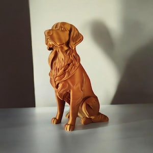 May include: A golden-colored dog statue in a sitting position. The statue has detailed fur and a regal posture, with its head held high. The sculpture is made of a solid material and is displayed on a white surface.