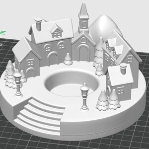 May include: A white, 3D-printed miniature village scene. The circular base features a series of steps, houses, a church, trees, and street lamps. A central circular opening is present. The overall design evokes a winter holiday theme.