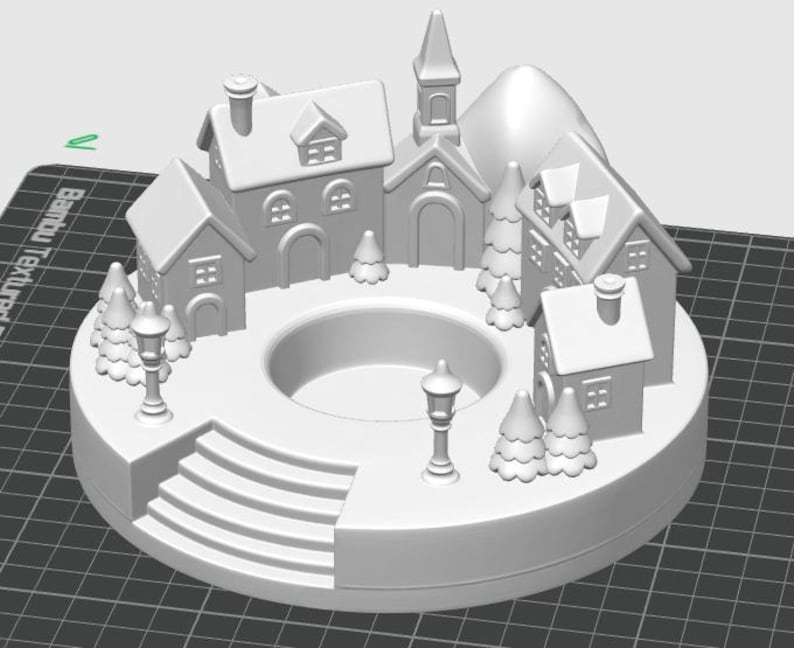 May include: A white, 3D-printed miniature village scene. The circular base features a series of steps, houses, a church, trees, and street lamps. A central circular opening is present. The overall design evokes a winter holiday theme.