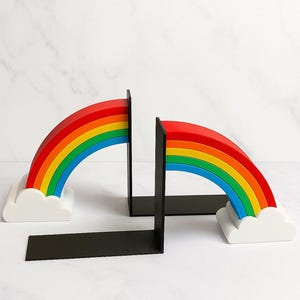 Puede incluir: Soportes para libros con forma de arco&iacute;ris. Cada uno presenta un dise&ntilde;o de arco&iacute;ris con arcos rojos, naranjas, amarillos, verdes, azules e &iacute;ndigo. El arco&iacute;ris se asienta sobre una base de nube blanca, con un soporte rectangular negro.