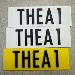 Pu&ograve; includere: Tre targhe rettangolari. Due sono bianche e una &egrave; gialla. Ogni targa riporta la scritta "THEA 1" in lettere nere e in grassetto. Le targhe sono disposte orizzontalmente, con quella gialla in basso.