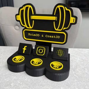 May include: Black and yellow dumbbell-shaped desk organizer with social media icons and the text "Prim3D & Creat3D". Features a Facebook, Instagram, and globe icon. Includes NFC symbols. Made of plastic.