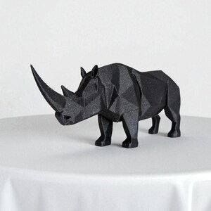May include: A black, geometric rhino sculpture with a textured surface. The rhino is standing on a white surface. The sculpture has a large horn and is a modern decorative piece.