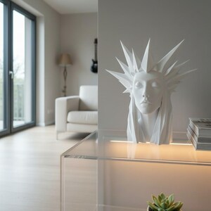 May include: A white sculpture of a woman's head with a spiky crown, set on a clear glass table. The sculpture has closed eyes and flowing hair. The background includes a white sofa, a guitar, and a window.