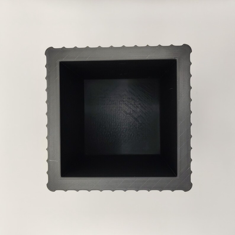 May include: A square, dark gray planter with a textured exterior and a smooth, black interior. The planter has a decorative, ridged border around the top edge. The interior dimensions appear to be approximately 6 inches square.