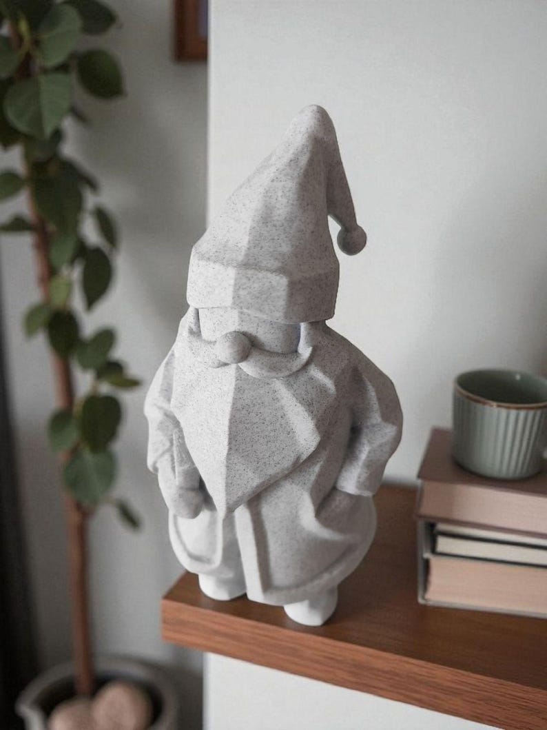 K&ouml;nnte beinhalten: Eine graue Zwergstatue mit spitzem Hut und langem Bart. Der Zwerg steht auf einem Holzregal. Eine gr&uuml;ne Pflanze und eine Tasse befinden sich im Hintergrund.