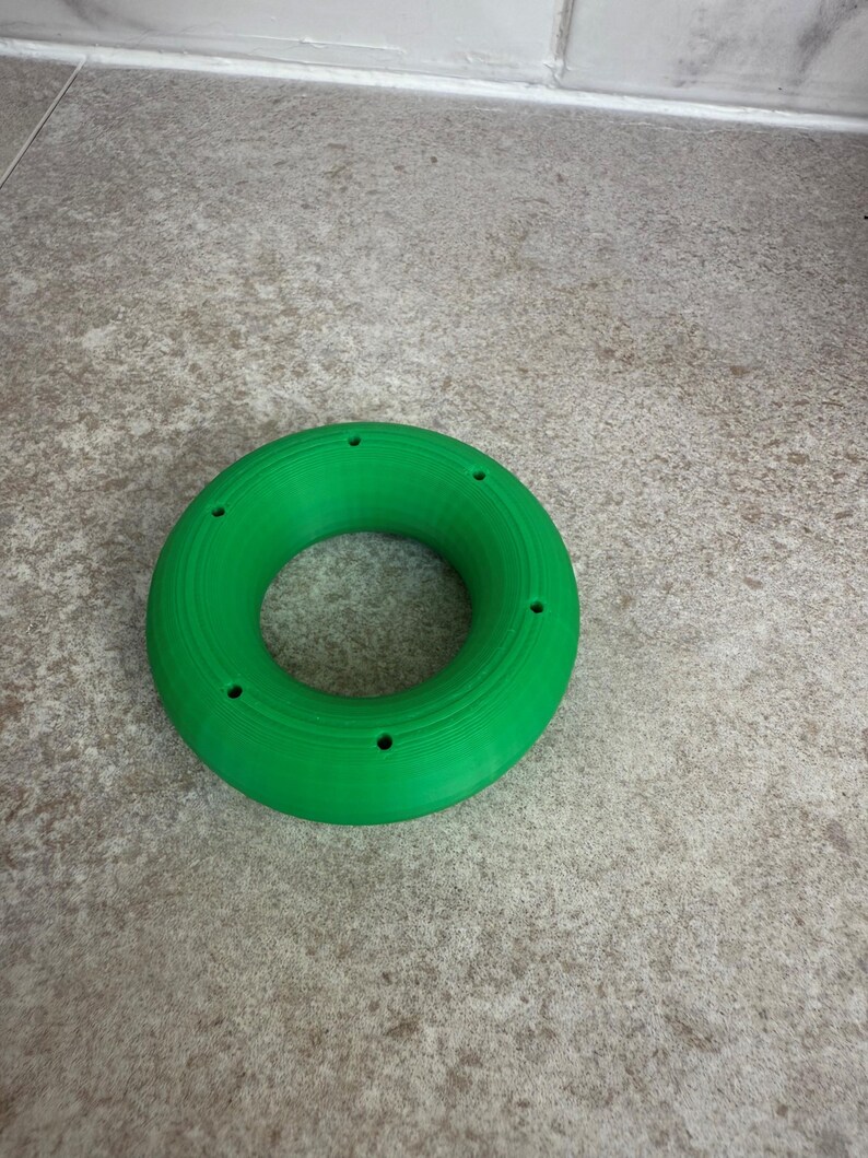 May include: A vibrant green ring with a series of small holes around its edge. The object, made from a solid material, is displayed on a neutral surface. The design is simple and geometric. The ring's diameter is approximately 10 cm.