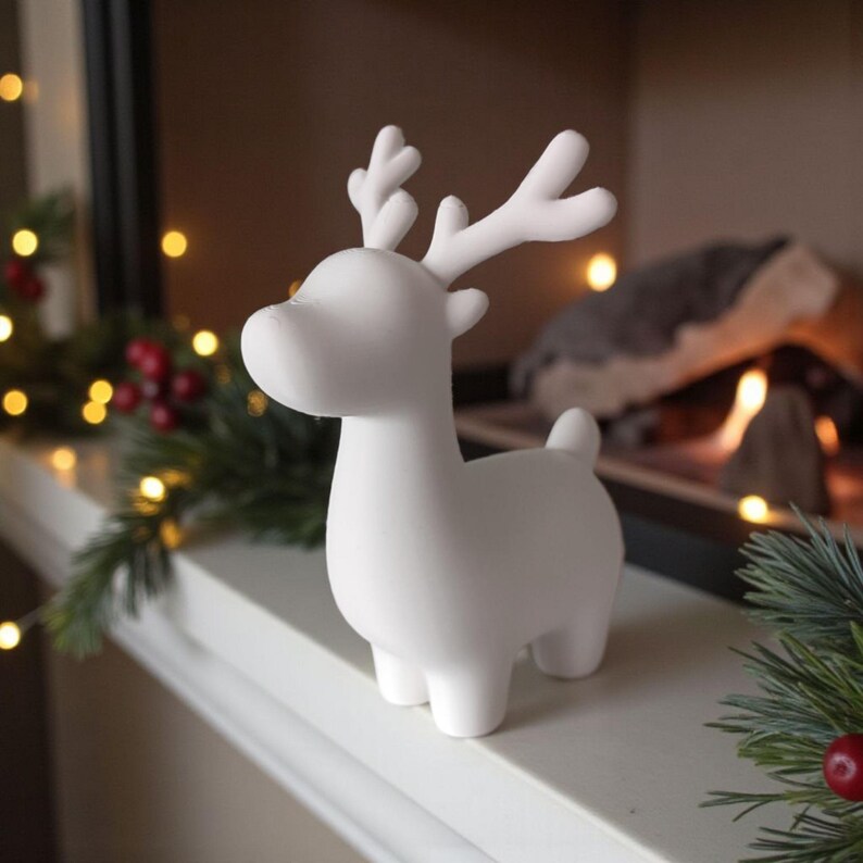 May include: A white ceramic reindeer figurine with antlers. The reindeer is standing on a white surface, with Christmas decorations in the background. The figurine is a decorative item for the holiday season.