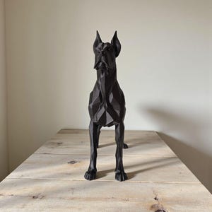 Puede incluir: Escultura geom&eacute;trica negra de un gran dan&eacute;s. La estatua del perro est&aacute; sobre una mesa de madera. La escultura tiene un dise&ntilde;o facetado, lo que le da un aspecto moderno y angular. Las orejas del perro est&aacute;n erguidas.