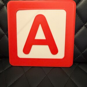 May include: A red and white square block featuring the letter "A". The letter "A" is in a bold, sans-serif font and is centered on a white background. The block has a red border, and the overall design is simple and clean. This block is likely used for educational purposes.