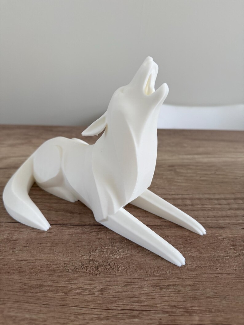 May include: A white, stylized sculpture of a howling wolf. The wolf is depicted in a seated position with its head raised and mouth open. The sculpture is made of a smooth, solid material and sits on a wooden surface.