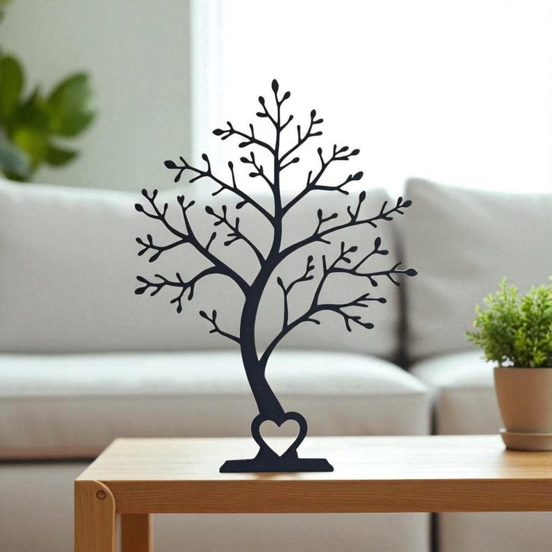 May include: A black metal tree-shaped jewelry holder with a heart-shaped cutout at the base. The tree has many branches and is displayed on a wooden table. A small potted plant is to the right.
