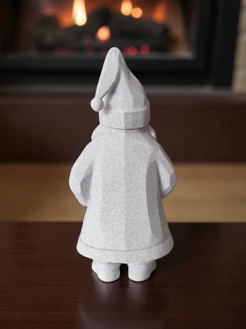 K&ouml;nnte beinhalten: Kleine, wei&szlig;e Zwergfigur mit spitzer M&uuml;tze und rundem Bommel. Der Zwerg tr&auml;gt einen langen Mantel und Stiefel. Die Figur besteht aus einem strukturierten Material und steht auf einer dunkelbraunen Oberfl&auml;che. Im Hintergrund ist ein Kamin zu sehen.