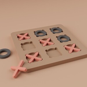 K&ouml;nnte beinhalten: Holz-Tic-Tac-Toe-Spiel mit beigem Brett, grauen Ringen und rosa X'en. Ein grauer Ring und ein rosa X sind au&szlig;erhalb des Bretts platziert. Ein klassisches Spiel.