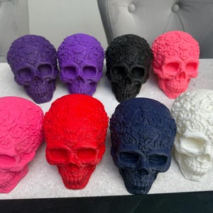 May include: A collection of decorative skull figurines in various colors, including purple, black, pink, red, navy blue, and white. Each skull features intricate floral patterns on the surface, creating a unique and artistic design.