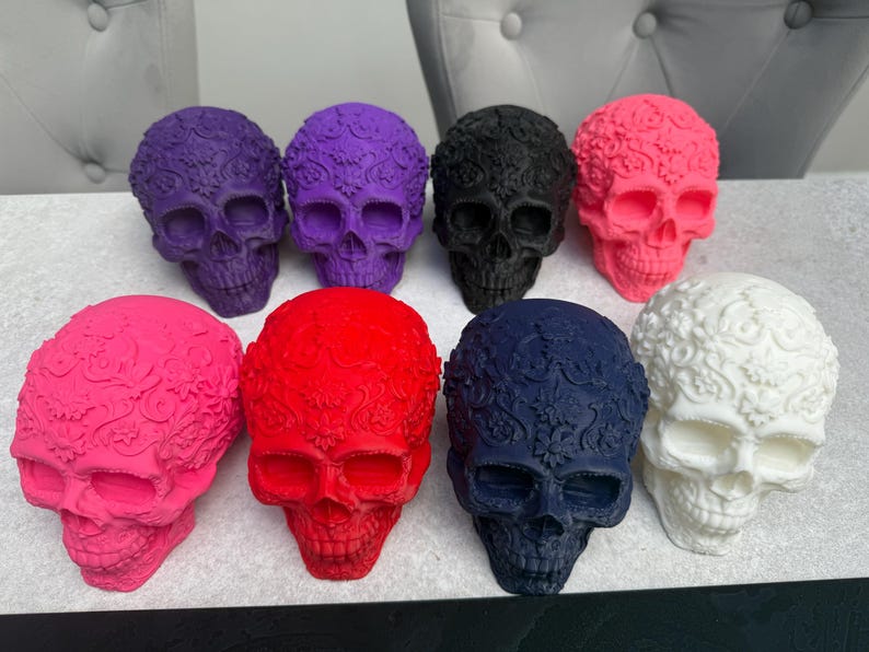 May include: A collection of decorative skull figurines in various colors, including purple, black, pink, red, navy blue, and white. Each skull features intricate floral patterns on the surface, creating a unique and artistic design.