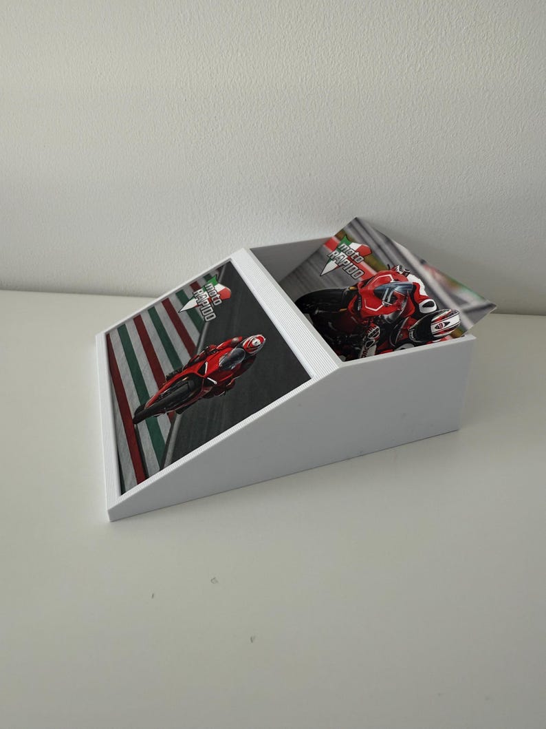 May include: White desk organiser with a slanted top and a rectangular base. The organiser features a racing theme with images of red motorcycles on a track. The text "moto rapido" is visible on the images.