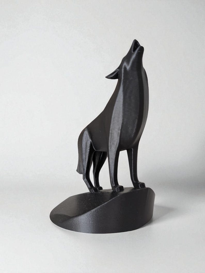 May include: A black sculpture of a howling wolf, standing on a small, rounded base. The wolf is depicted with its head raised and mouth open, in a stylized, modern design. The sculpture is made of a solid, matte black material.