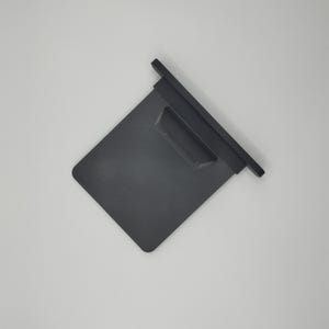 May include: A dark grey, rectangular object with a raised section and a lip. The object appears to be made of a solid material, possibly plastic or metal. The design is simple and functional.