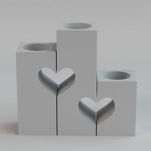 May include: A gray, tiered candle holder with heart cutouts. The holder has three sections of varying heights, each with a circular opening at the top for candles. The design features two heart-shaped cutouts.