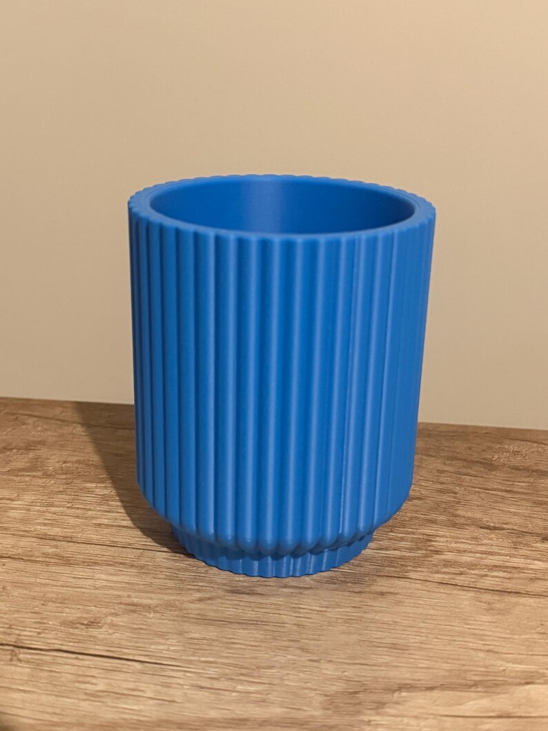May include: A vibrant blue cylindrical planter with vertical ribbed detailing. The planter has a slightly flared base and a smooth interior. The color is a bright, solid blue, suitable for indoor or outdoor use.