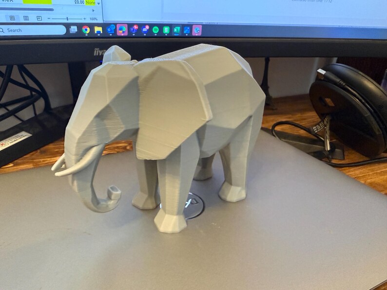 Op de afbeelding: Een lichtgrijze, geometrische olifantenfiguur. De olifant heeft een facetontwerp, met zichtbare randen en vlakken, waardoor hij een moderne, hoekige uitstraling heeft. De slurf is gekruld en de slagtanden zijn zichtbaar. De figuur is een decoratief item.