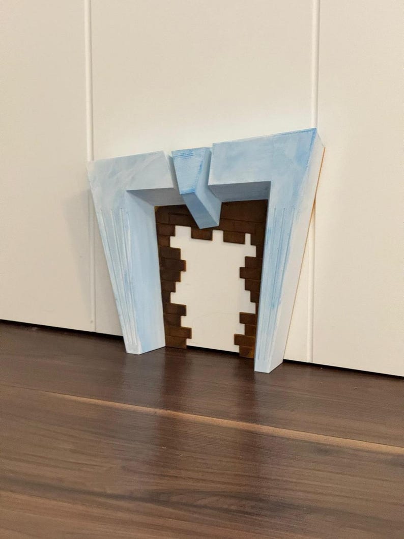 May include: A geometric, abstract sculpture with a light blue painted exterior and a brown and white interior. The sculpture is placed on a dark brown wooden surface, with a white wall in the background. The artwork has a modern, architectural aesthetic.