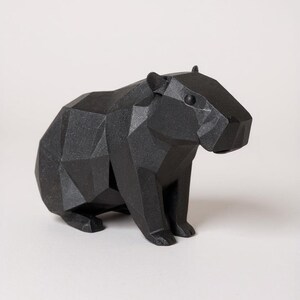 May include: A black geometric sculpture of a capybara. The capybara is depicted in a sitting position with a faceted, polygonal design. The sculpture is made of a matte black material and has a minimalist aesthetic.