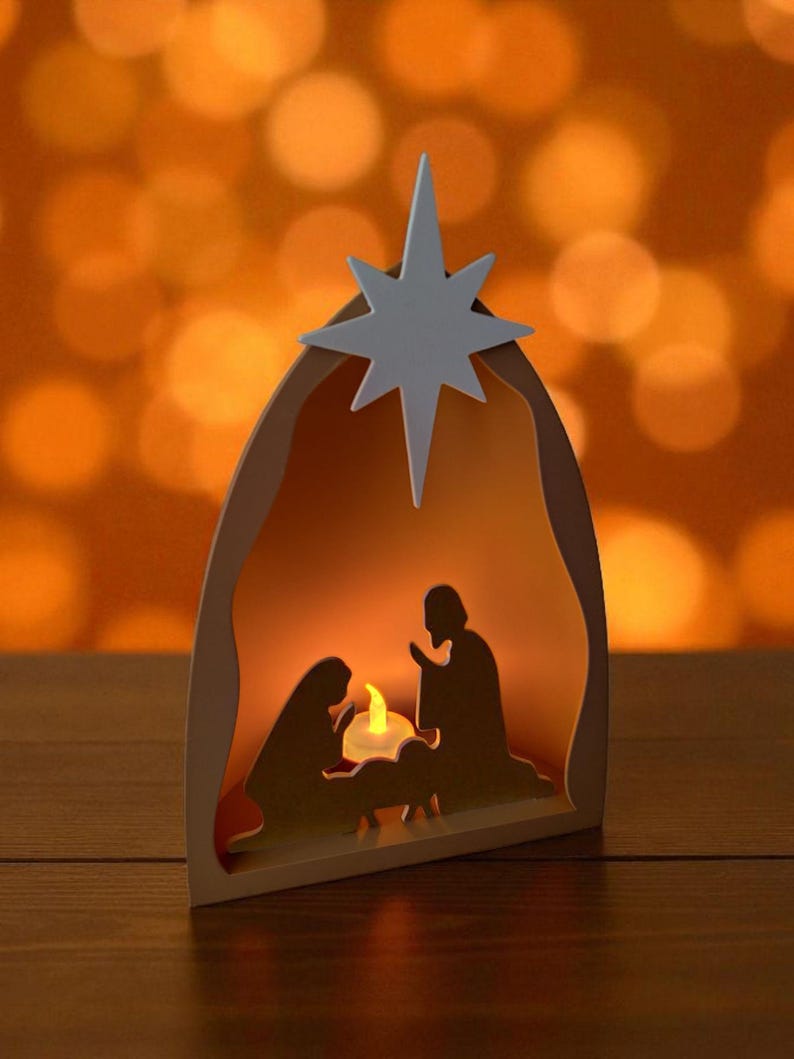 May include: A wooden nativity scene featuring a white star. The scene shows the silhouettes of Mary, Joseph, and baby Jesus, with a candle inside. The background is a warm orange colour.